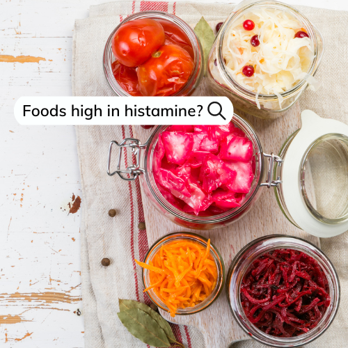 Jars of pickled cabbage, tomatoes, carrots and beetroot on a wooden board against a white bckground